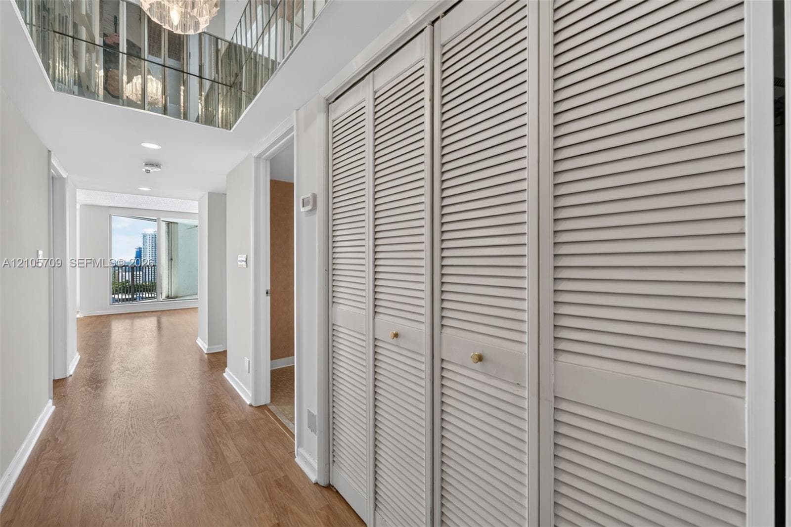 Open living area featuring wood-finish flooring, floor-to-ceiling glass sliding doors, a private balcony, and an overhead chandelier fixture
