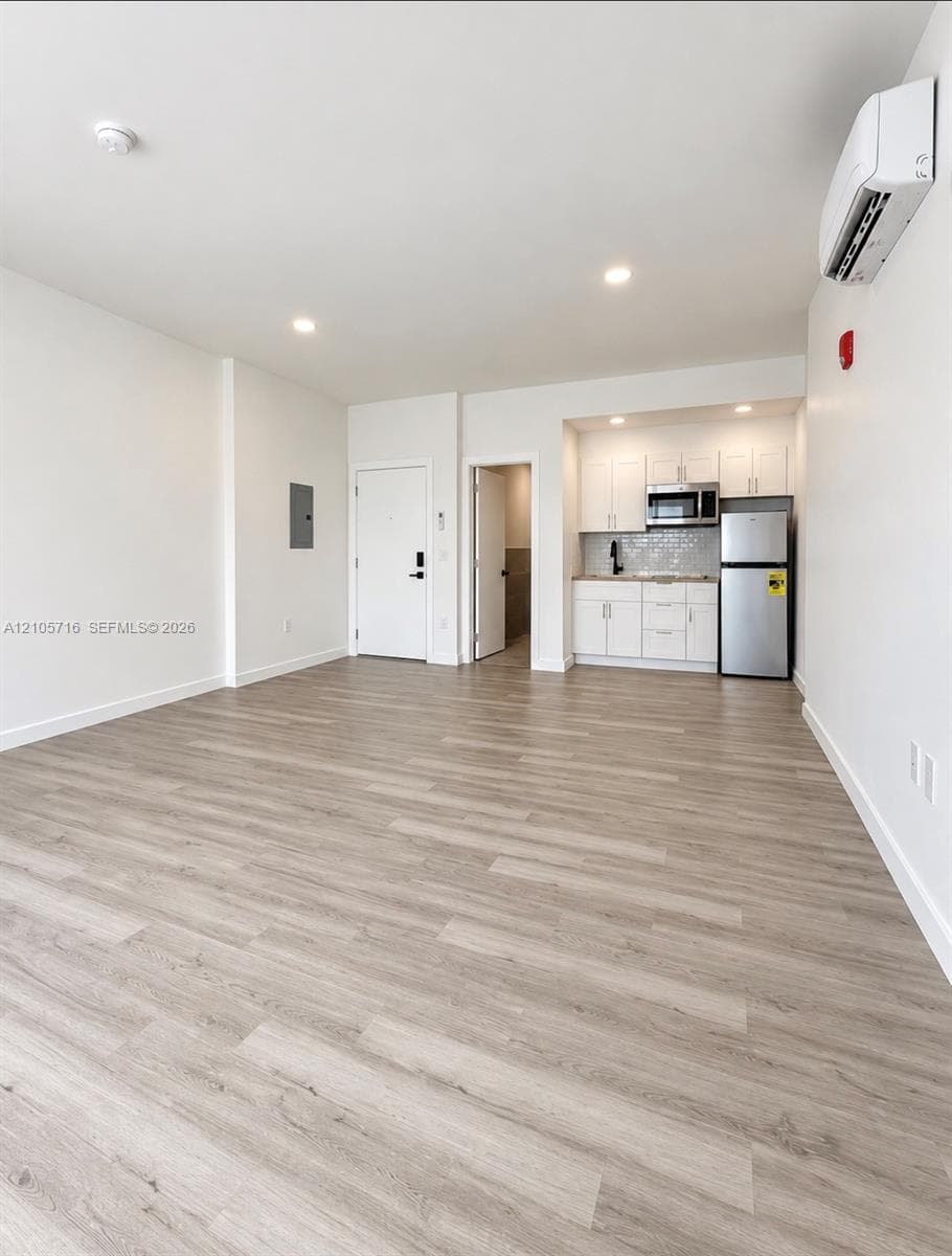 Open-concept interior featuring wood-finish flooring, recessed lighting, and wall-mounted climate control