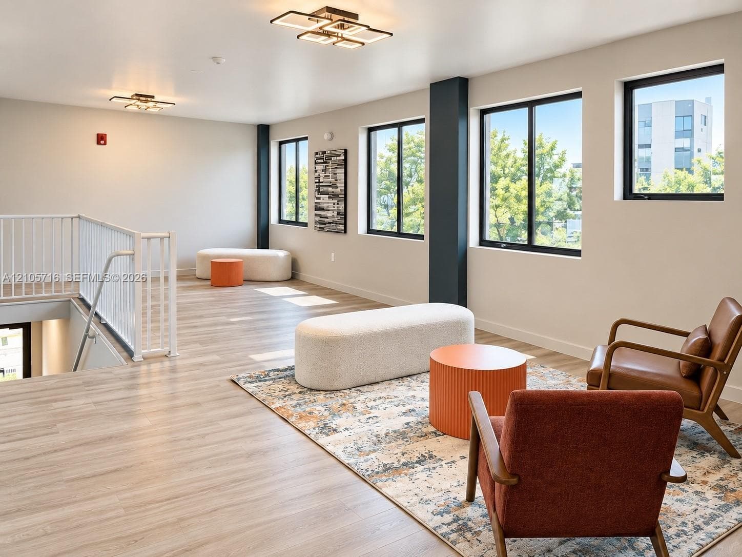 Open-concept LOBBY space featuring wood-finish flooring, geometric LED ceiling fixtures, large windows with black frames, and a white metal staircase railing