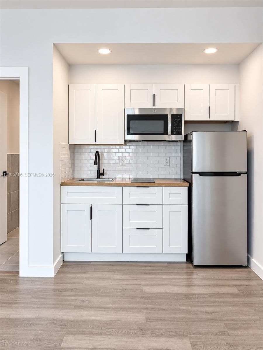 Kitchenette featuring white Shaker-style cabinetry, stainless steel appliances, subway tile backsplash, matte black hardware, and wood-finish flooring