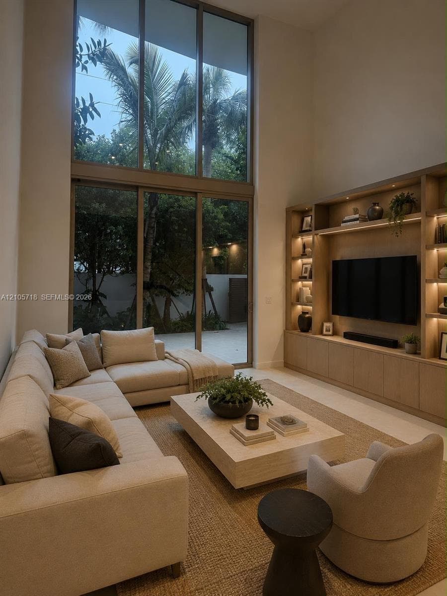 Double-height ceiling, floor-to-ceiling windows, and custom built-in wood shelving featuring integrated lighting