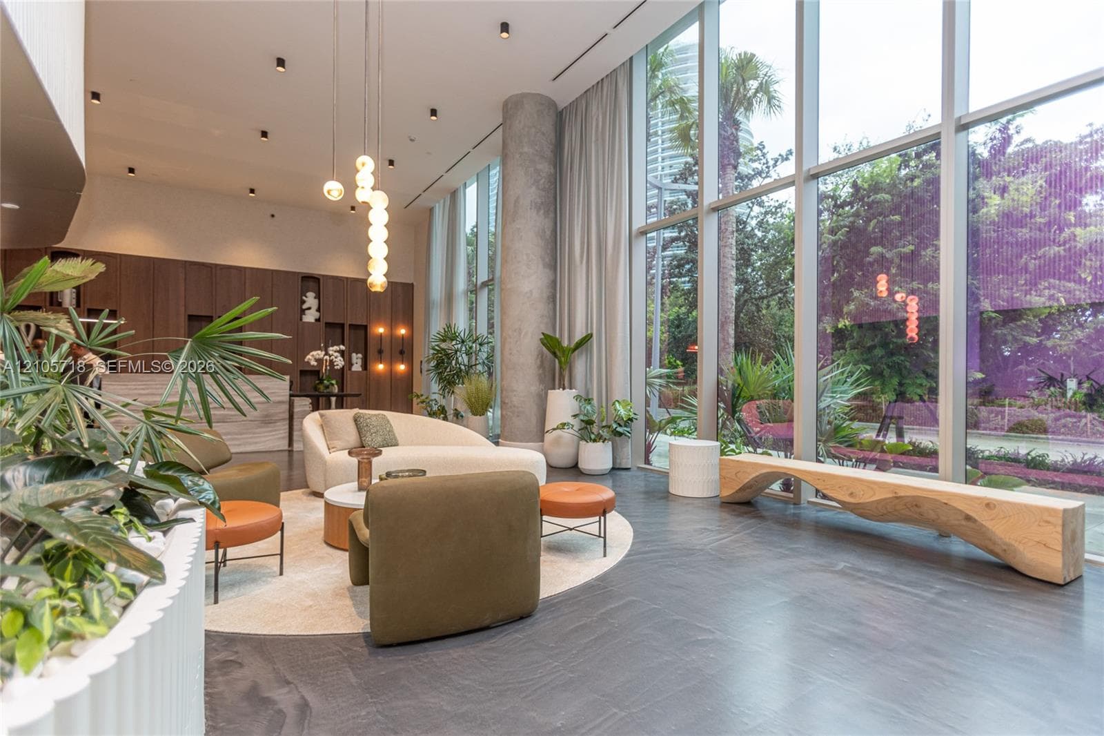 Double-height floor-to-ceiling windows, dark stone flooring, exposed concrete structural column, recessed ceiling lighting, and built-in wood-veneer cabinetry