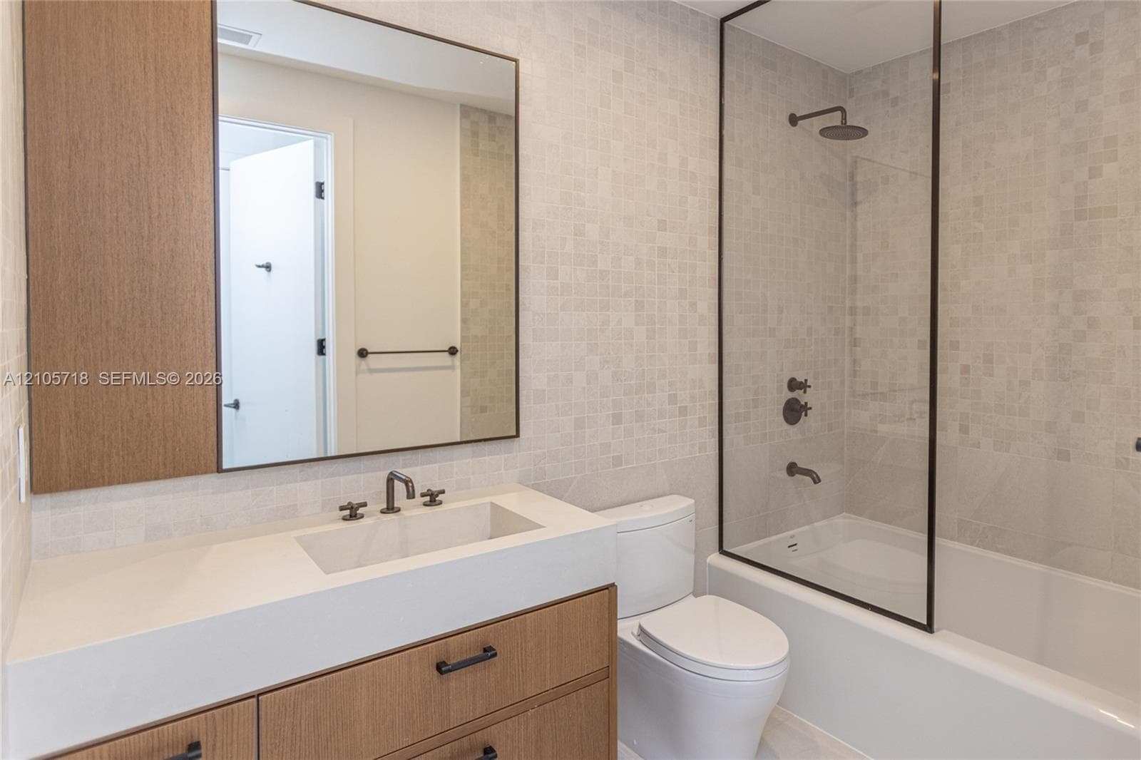 Modern vanity with wood-finish cabinetry, integrated countertop with rectangular basin, matte black plumbing fixtures, glass-enclosed shower, and mosaic tile wall accents