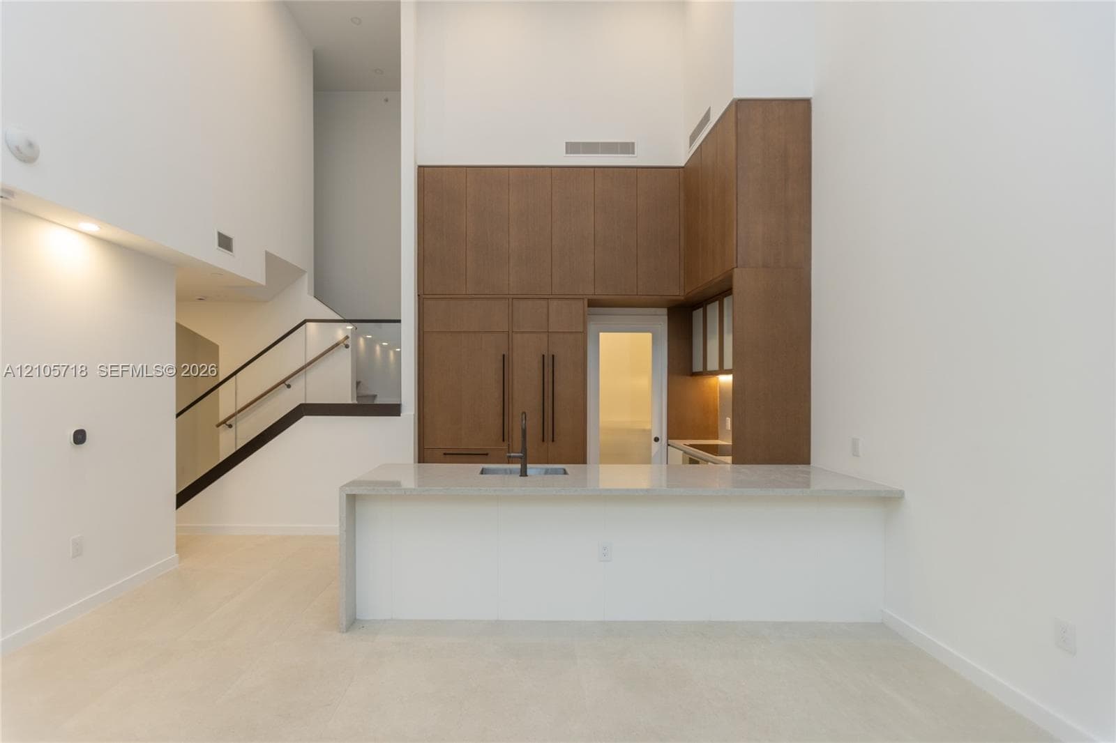 Kitchen featuring floor-to-ceiling wood-finish cabinetry, stone-surfaced waterfall island with integrated sink, and matte black hardware