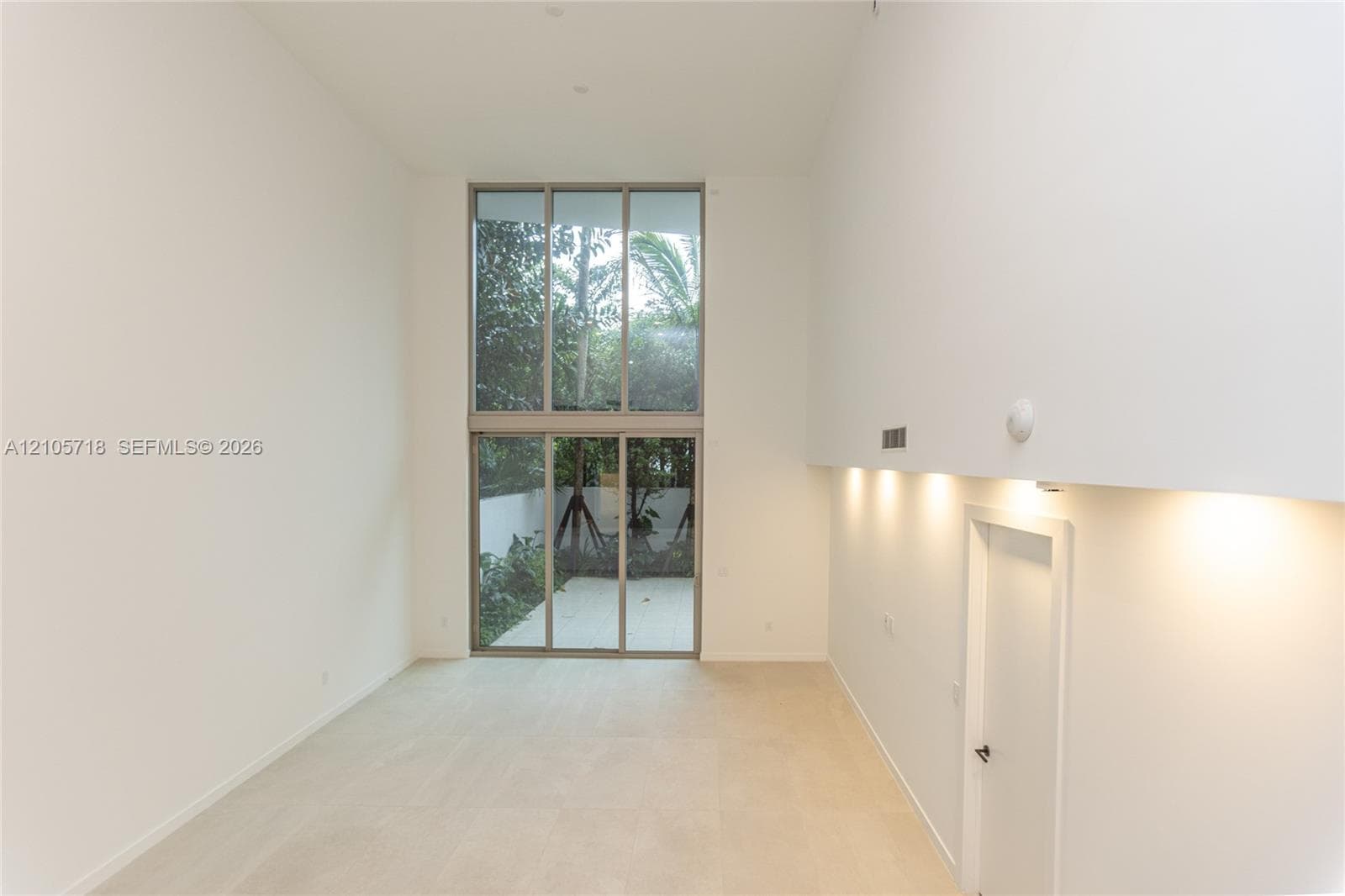 Double-height ceilings, expansive floor-to-ceiling windows, light-toned stone flooring, and integrated recessed wall lighting