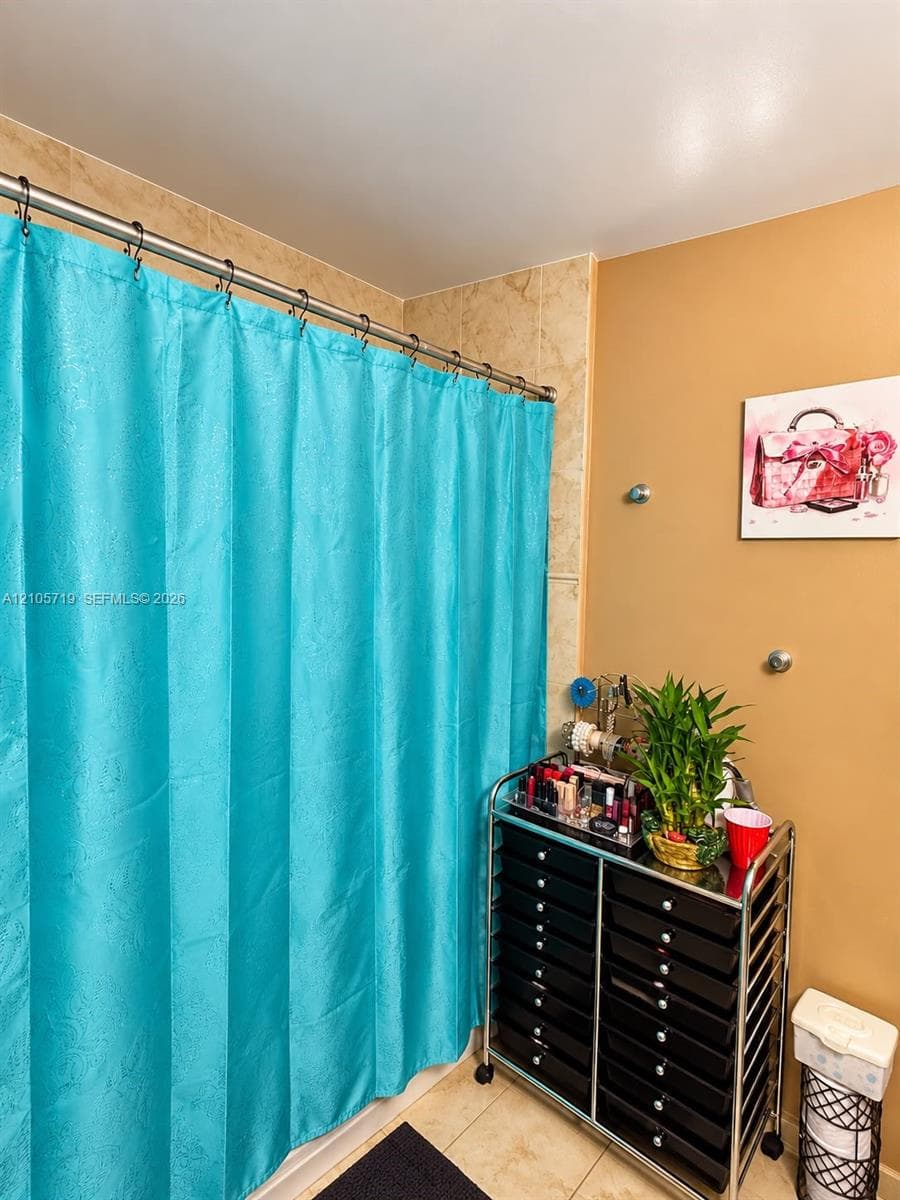Stone-finish tile shower surround with a metal curtain rod and neutral wall tones