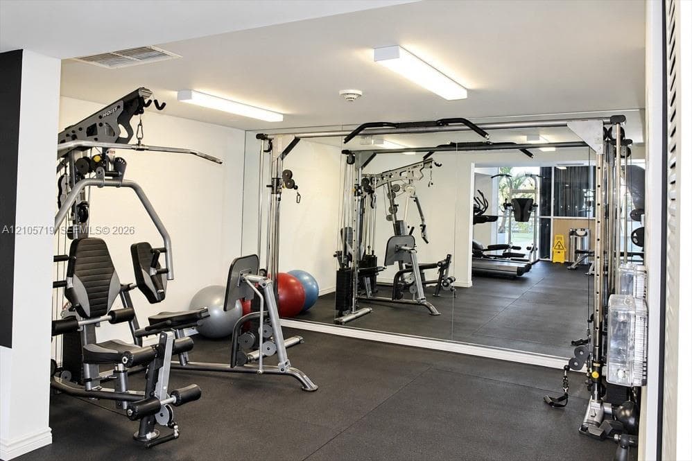Fitness center featuring wall-to-wall mirrors, durable rubberized flooring, and dual overhead linear lighting fixtures