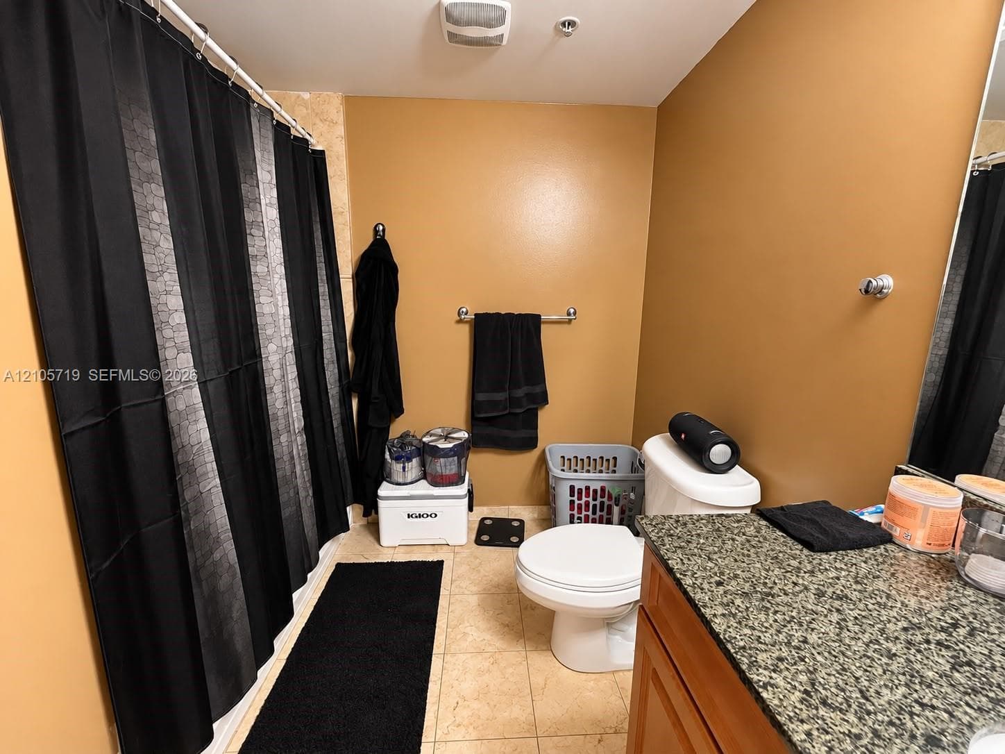 Bathroom featuring a vanity with a stone-finish countertop, neutral tile flooring, and a tub enclosure