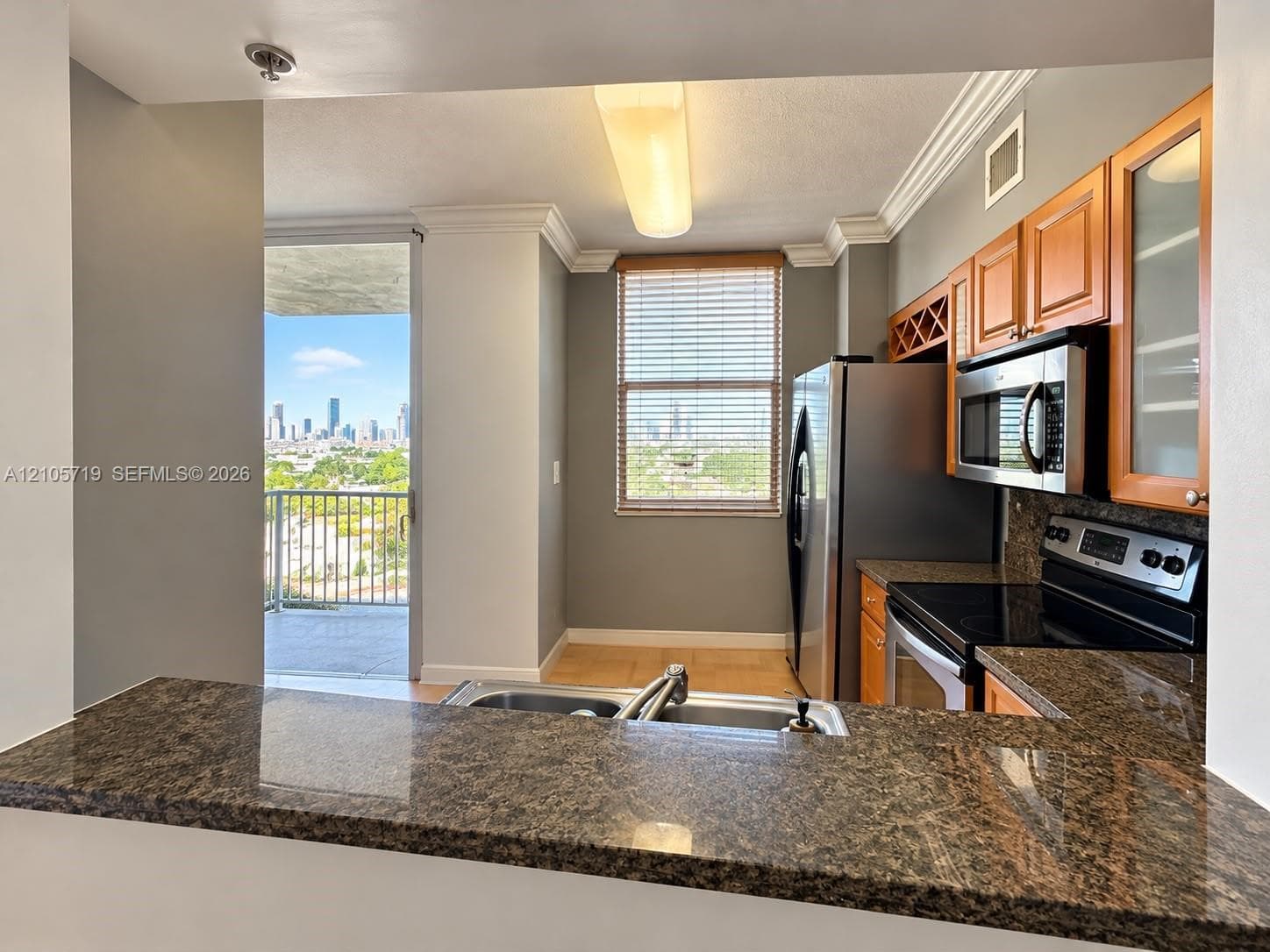 Kitchen featuring a granite countertop peninsula, natural wood cabinetry with glass-front display panels, stainless steel built-in microwave, and crown molding