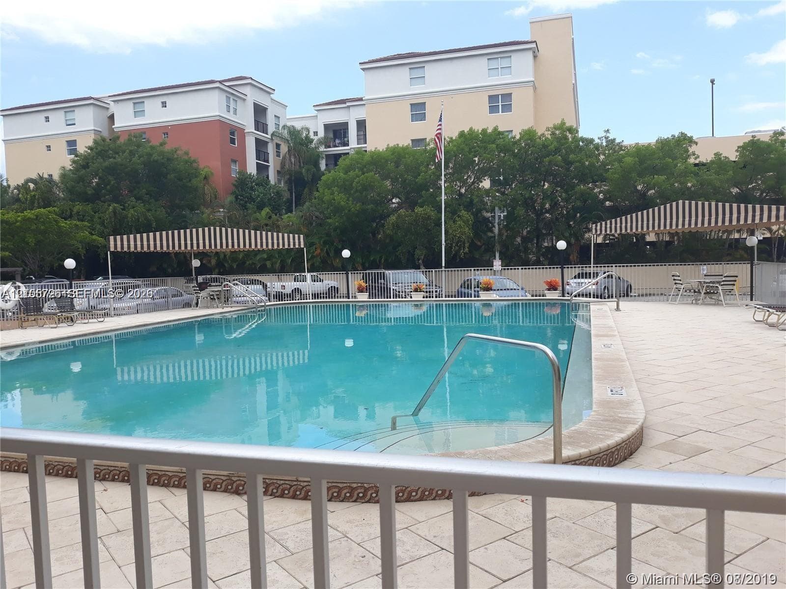 Rectangular swimming pool featuring a tiled deck, metal handrails, and striped architectural awnings