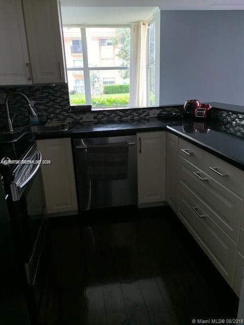 Kitchen featuring light-toned cabinetry, dark stone countertops, mosaic tile backsplash, stainless steel appliances, and large-format window