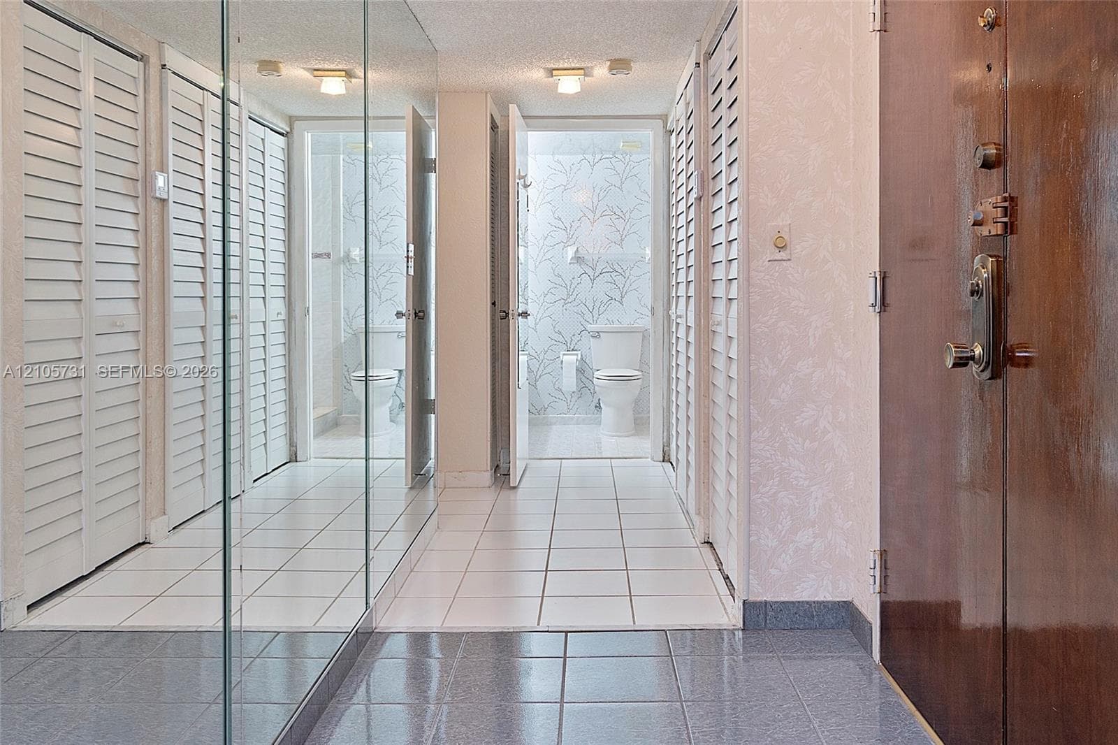 Hallway featuring floor-to-ceiling mirror paneling, white louvered closet doors, square tile flooring, and flush-mount ceiling lighting