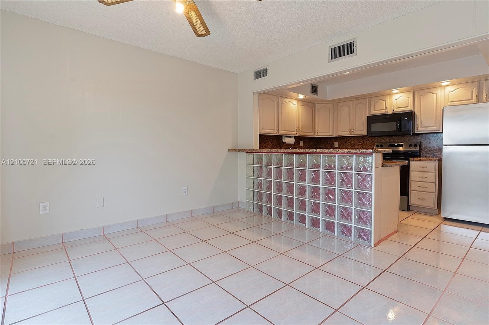 Kitchen area featuring a glass block breakfast bar, ceramic tile flooring, neutral cabinetry, stone-finish countertops, and stainless steel appliances