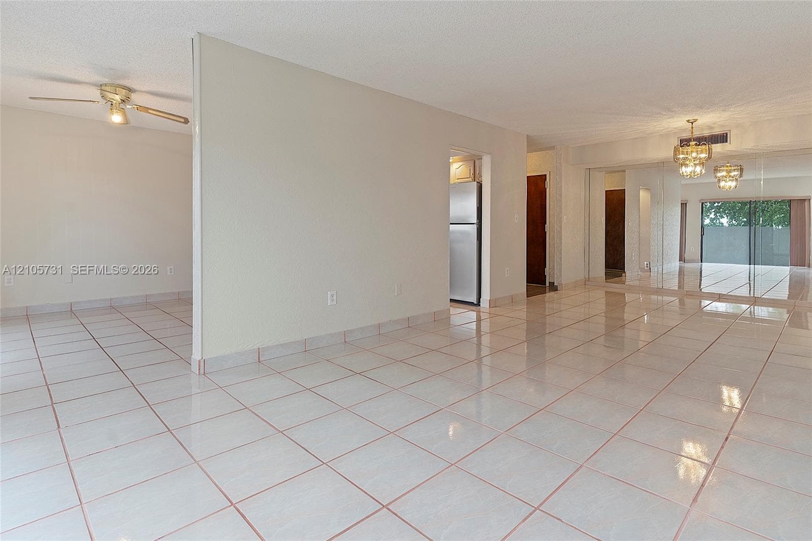 Open-concept interior featuring light-toned tile flooring, mirrored sliding closet doors, a dual-arm ceiling fan, and ornate overhead lighting fixtures