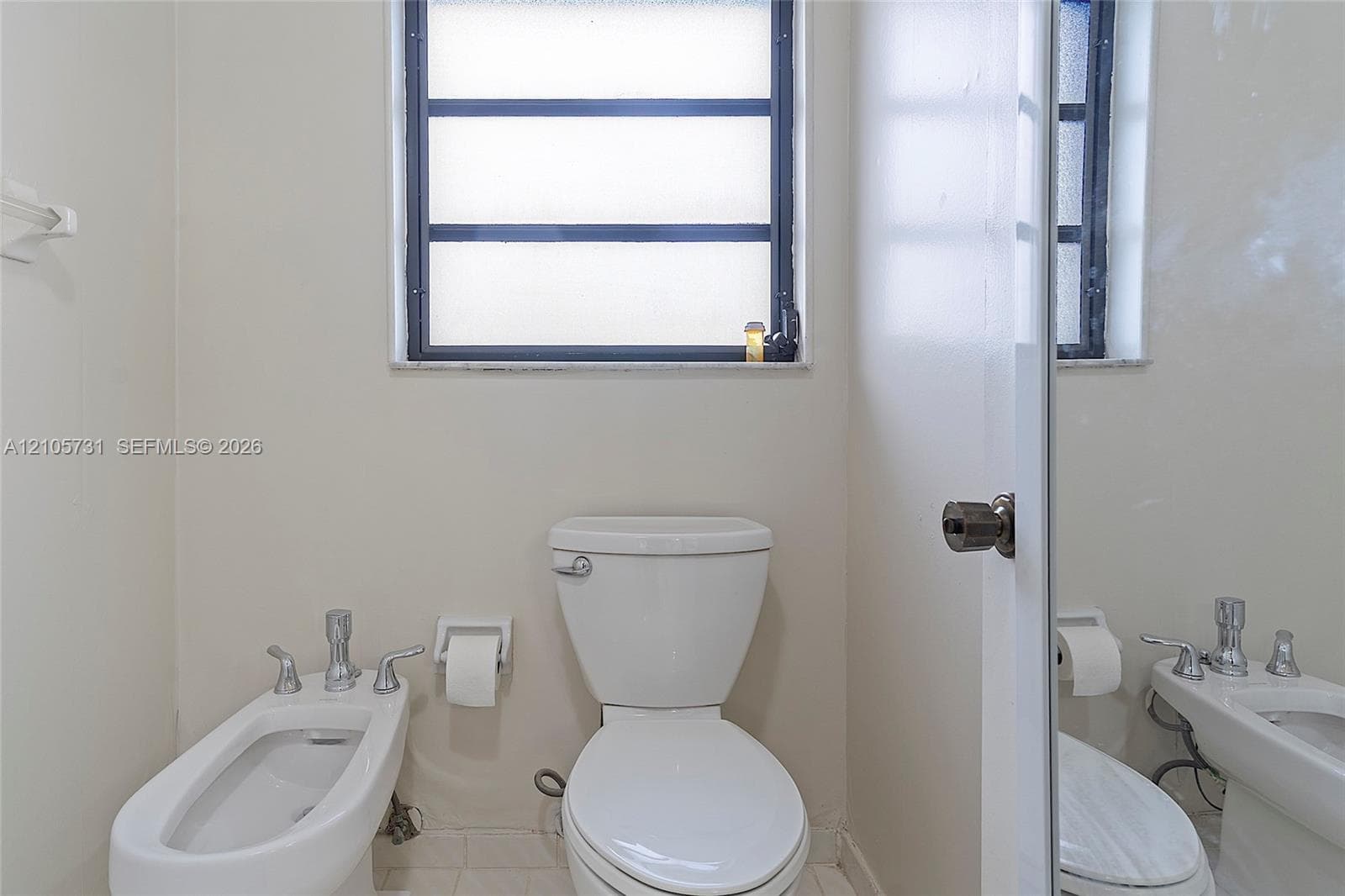 White ceramic toilet, bidet with chrome faucet hardware, and horizontal-pane window with dark frame