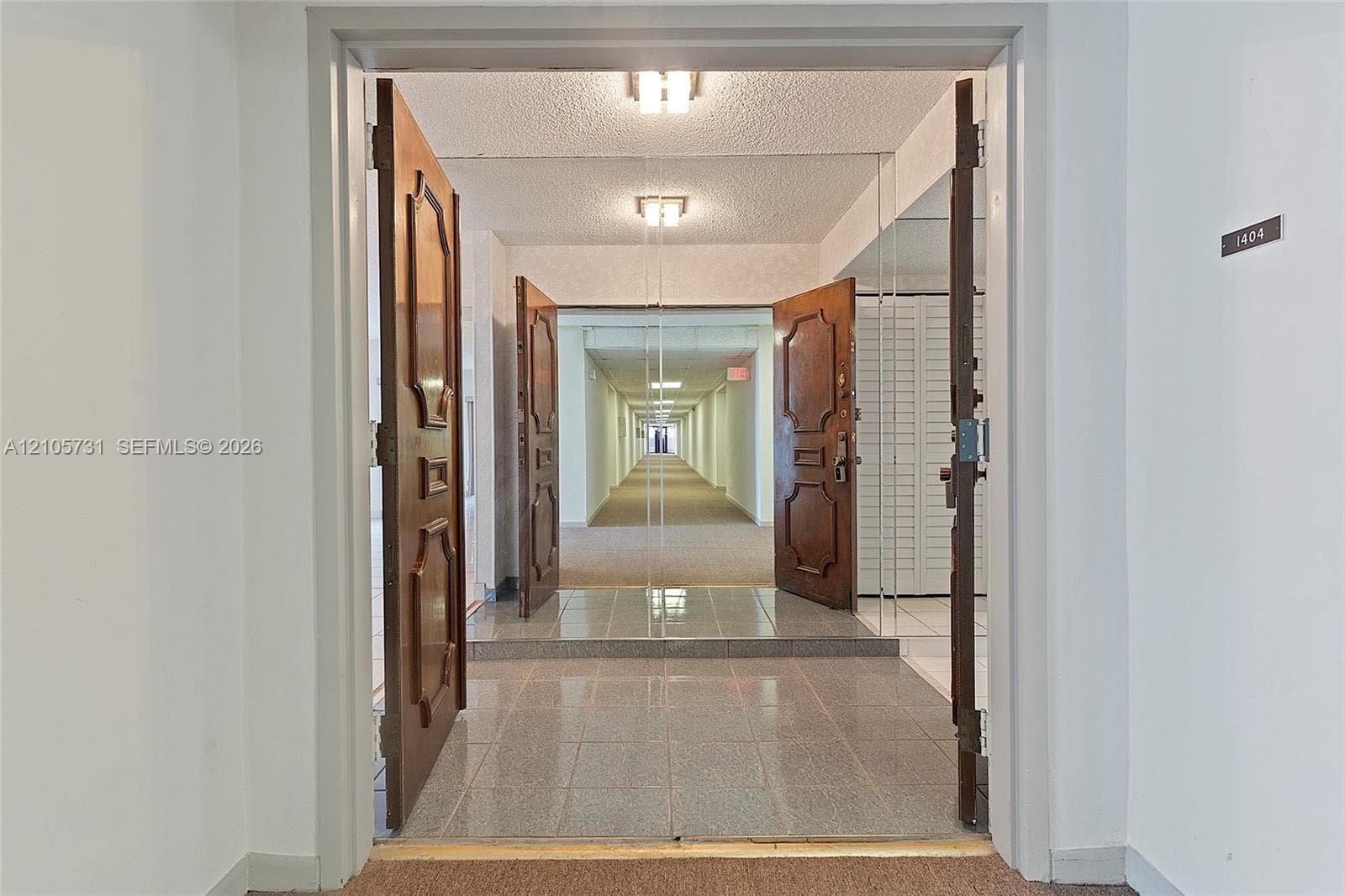Entryway featuring double solid-wood doors with decorative panels, polished stone-finish floor tiling, and integrated wall-to-wall mirror paneling