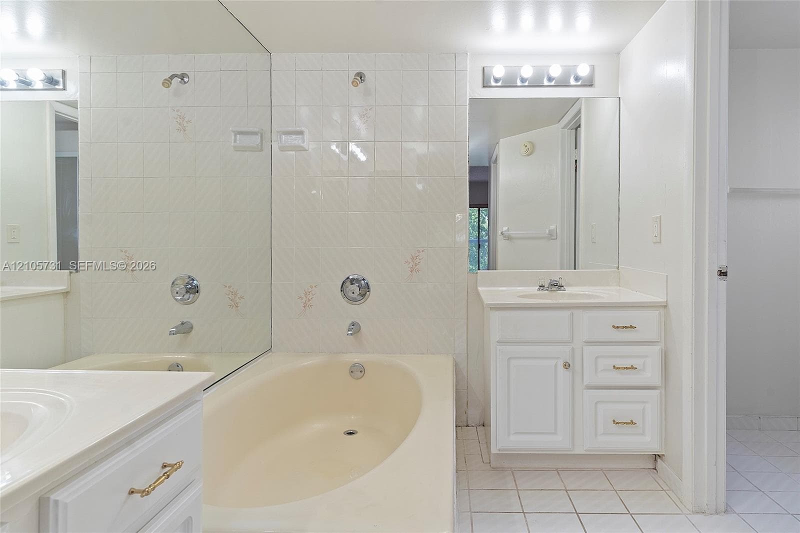 Bathroom featuring a vanity with integrated sink, porcelain tile flooring, full-width wall mirror, and a bathtub with tiled surround