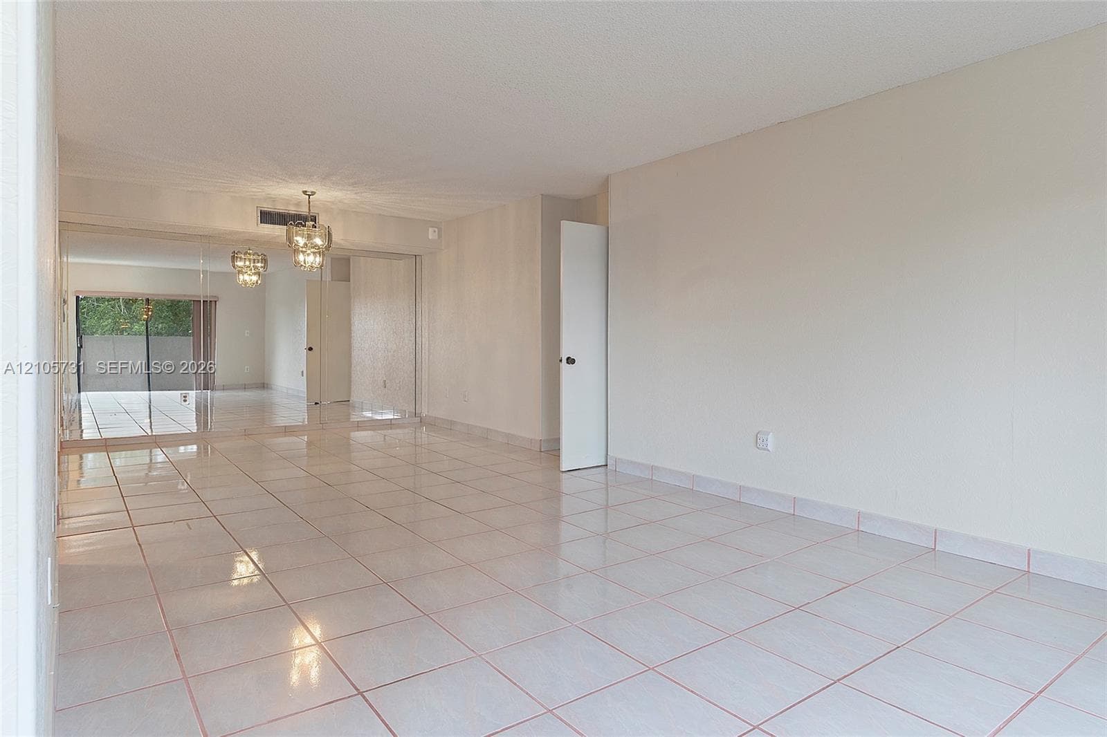Neutral-toned interior space featuring light-colored ceramic tile flooring, mirrored wall panels, and a central crystal-style chandelier