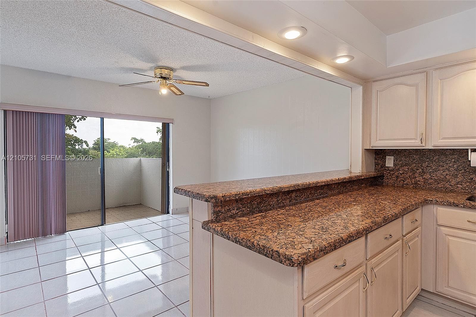 Kitchen featuring cabinetry with crown molding, stone-finish countertops, recessed lighting, white tile flooring, and a sliding glass door