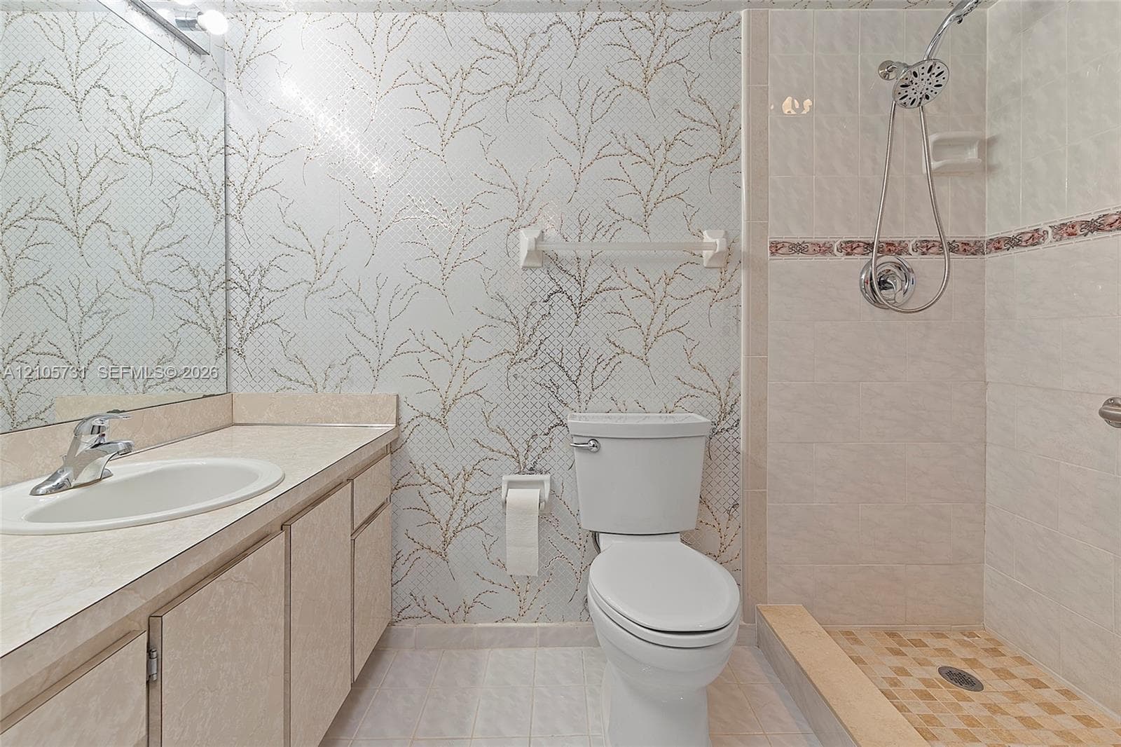 Bathroom featuring a vanity with an integrated sink, patterned wall covering, floor-to-ceiling mirror, and a walk-in shower with a handheld fixture and decorative tile accent border