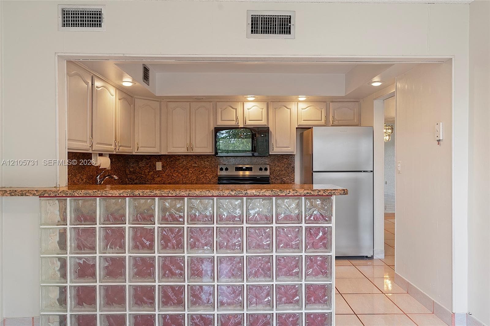 Kitchen featuring white cabinetry, stone-finish countertops, stainless steel appliances, and a glass block breakfast bar