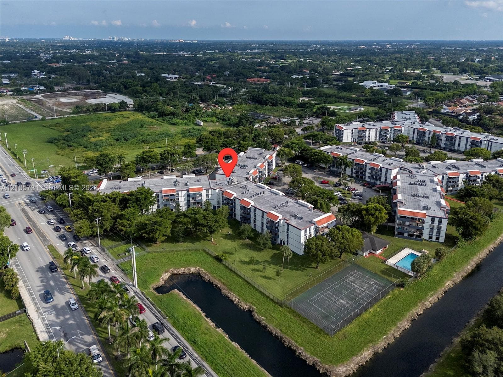 Aerial perspective of multi-story residential complex featuring an outdoor swimming pool, tennis court, and manicured lawn areas