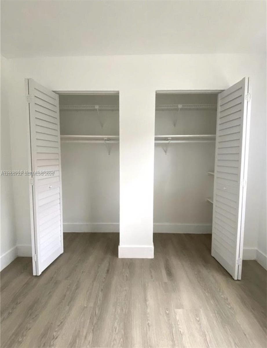 Dual reach-in closets featuring white louvered bifold doors, integrated wire shelving, and wood-finish flooring