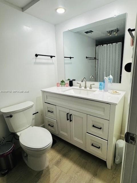 Bathroom featuring a vanity with white cabinetry, a solid-surface countertop, an integrated rectangular sink, matte black hardware, and wood-finish flooring