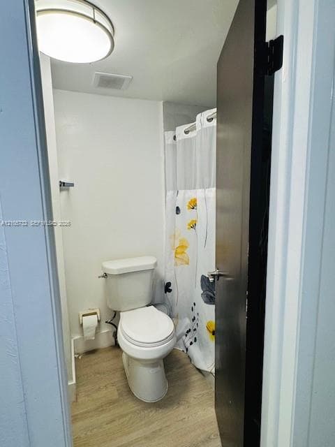 Bathroom featuring wood-finish flooring, a white elongated toilet, and a dome-style ceiling light fixture
