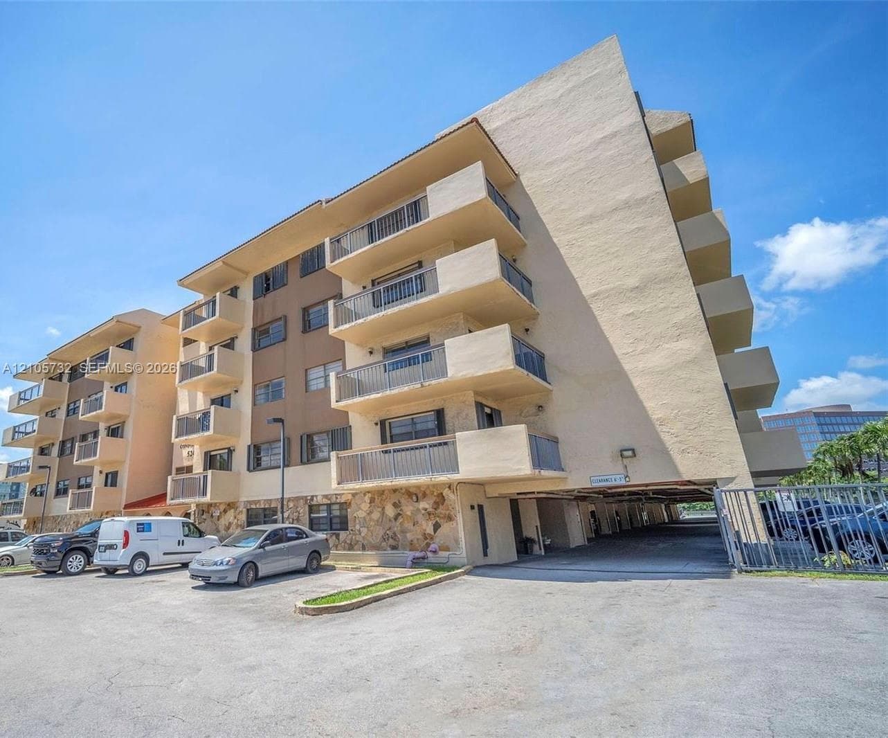 Multi-story exterior featuring stone veneer accents, private balconies with metal railings, and a covered ground-level parking area