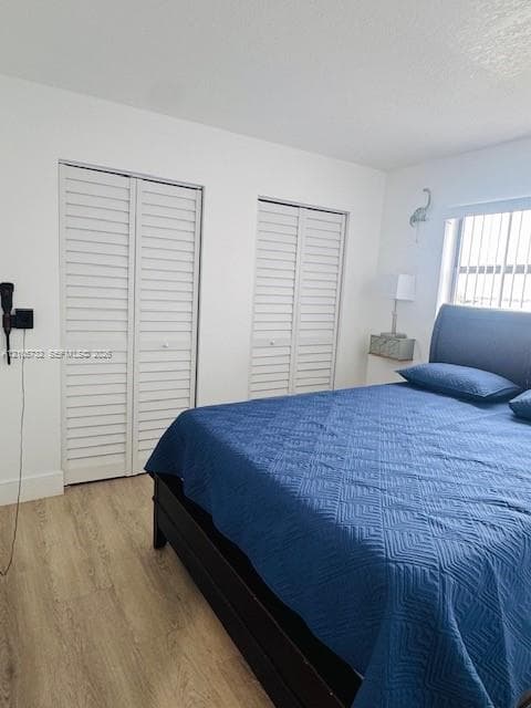 Neutral wall tones with wood-finish flooring, dual bi-fold louvered closet doors, and wall-mounted lighting fixture