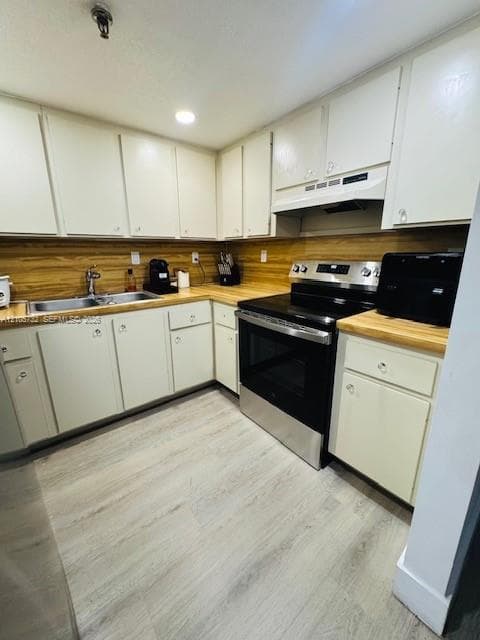 Kitchen featuring flat-panel cabinetry, wood-finish countertops, stainless steel range with overhead vent hood, dual-basin stainless steel sink, and light-toned wood-finish flooring