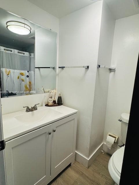 Bathroom featuring a white vanity cabinet with a integrated sink, large wall-mounted mirror, brushed-nickel hardware, and wood-finish flooring