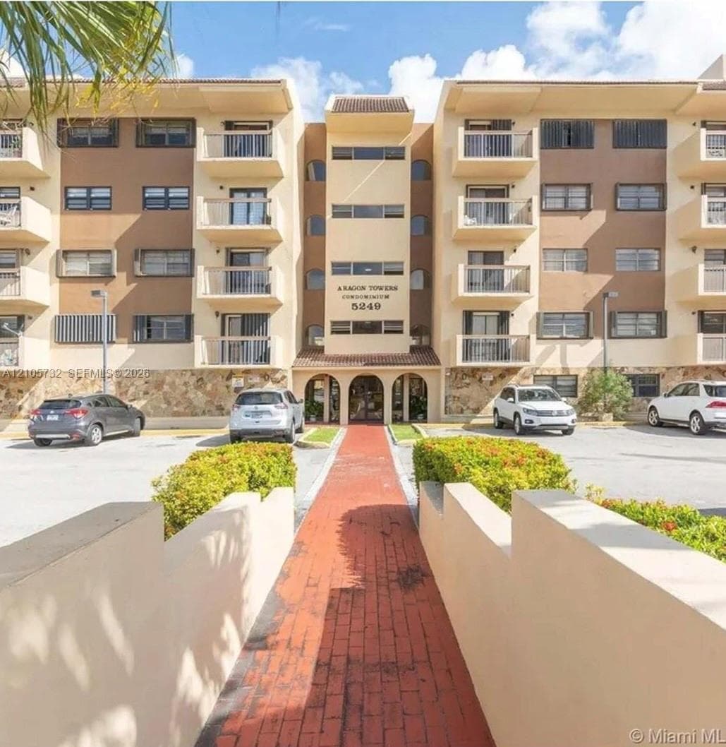 Multi-story condominium exterior featuring a stone-clad facade, private balconies, an arched entryway, and a paved brick walkway