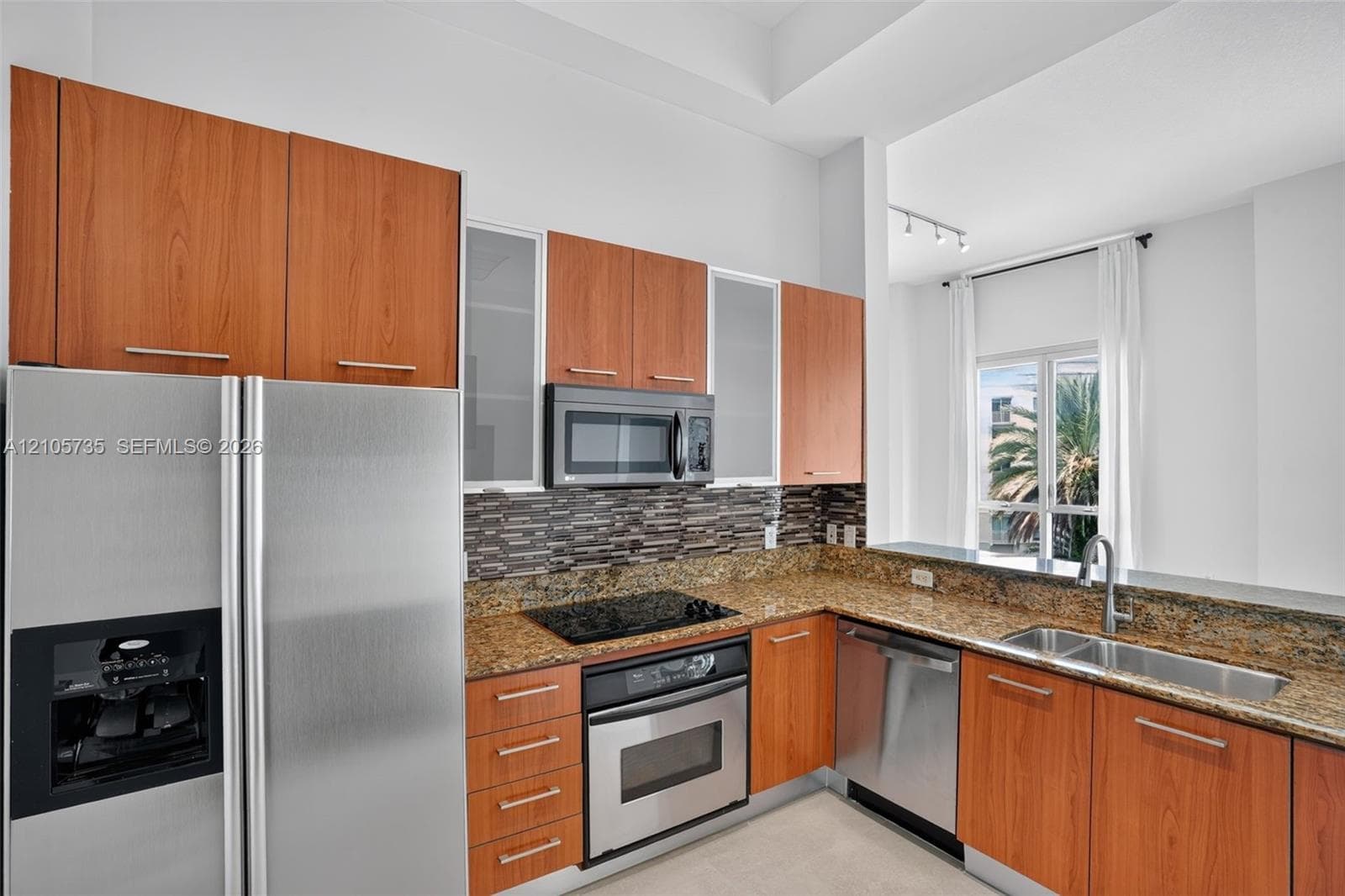 Kitchen featuring wood-finish cabinetry, stone countertops, a glass-tile backsplash, and a suite of stainless steel appliances