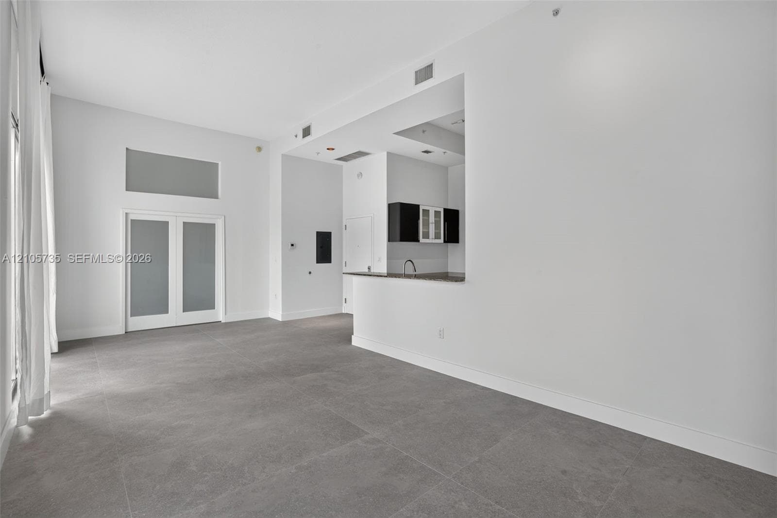 Open-concept interior featuring high ceilings, large-format tile flooring, double doors with frosted glass panes, and a pass-through kitchen counter with built-in cabinetry