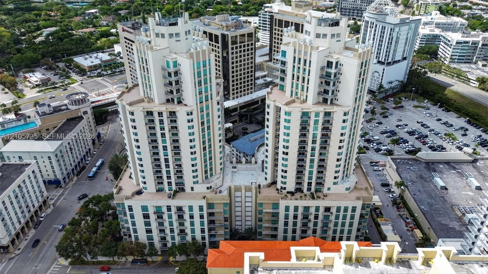 High-rise urban towers featuring light-toned masonry facades, multiple tiers of balconies, expansive grid-pattern windows, and a central podium terrace