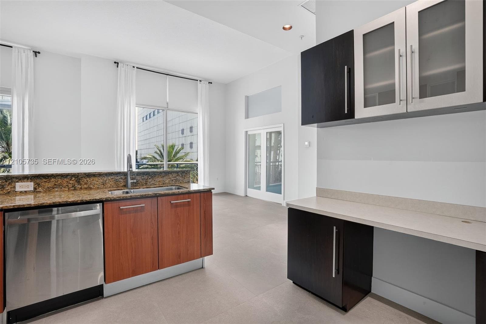 Kitchen featuring stone countertops, stainless steel dishwasher, dual-tone cabinetry with frosted glass inserts, and large-format tile flooring