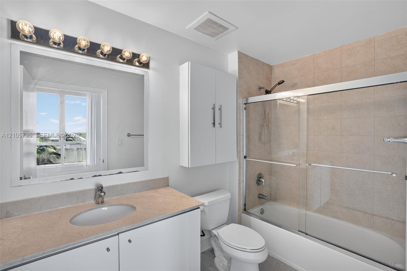 Bathroom featuring a vanity with a solid-surface countertop, an integrated oval sink, a wall-mounted storage cabinet, and a bathtub-shower combination with a glass sliding enclosure and stone-tile surround