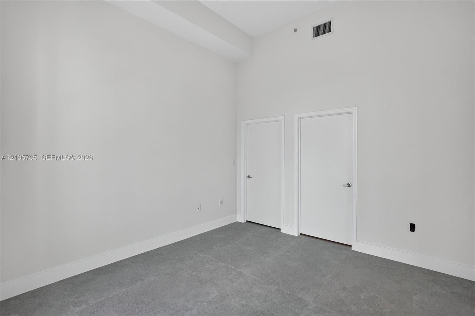 High-ceiling interior featuring matte neutral wall finishes, large-format tile flooring, and two flush-panel interior doors with brushed metallic hardware
