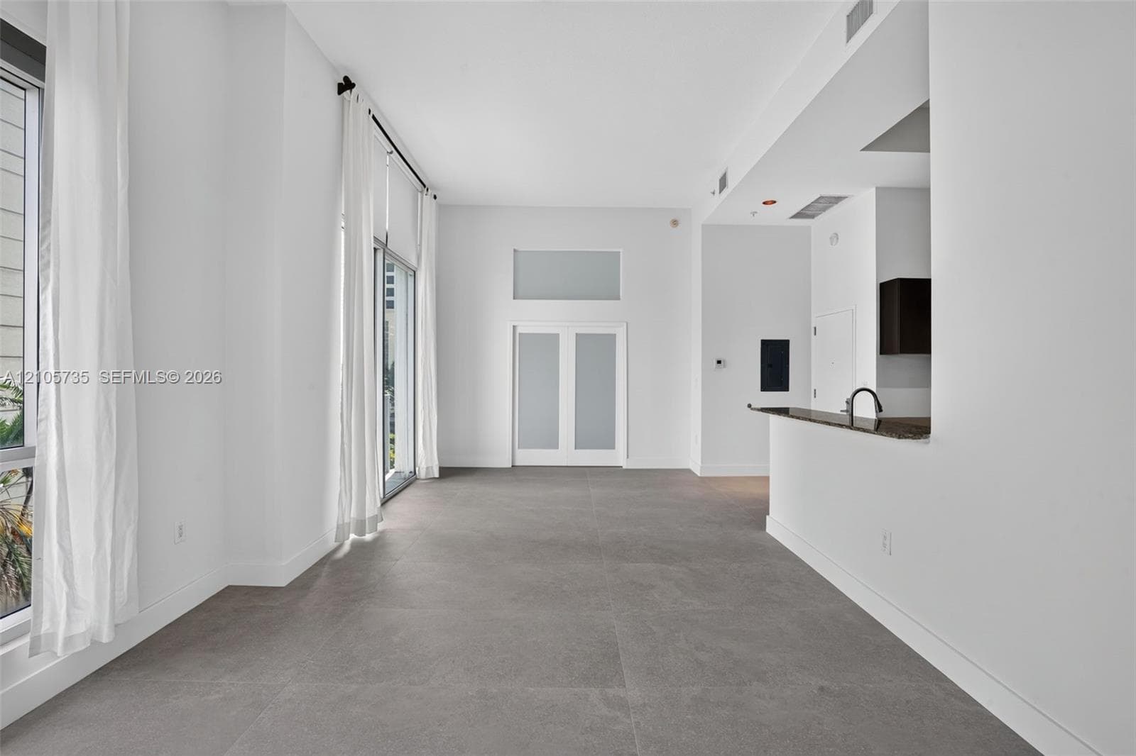 High-ceiling interior featuring full-height windows, large-format tile flooring, double doors with frosted glass panels, and a built-in counter with a sink