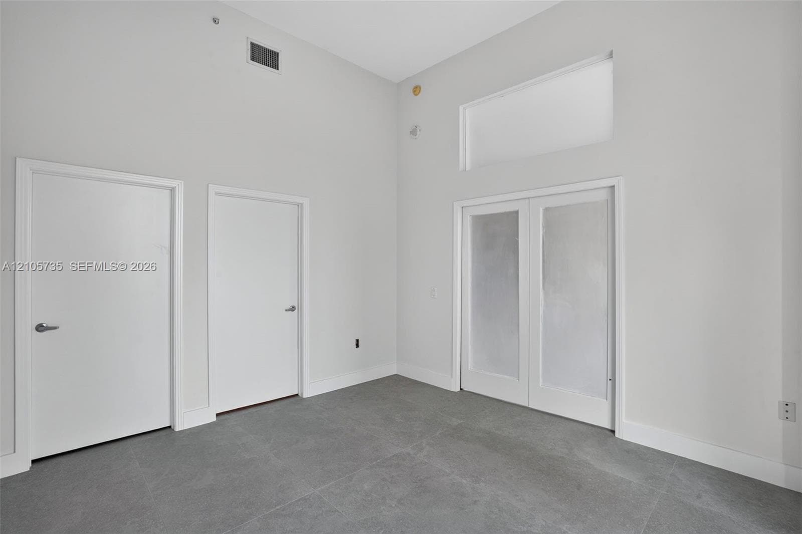 Vaulted ceilings, large-format grey tile flooring, double doors with frosted glass panes, and an oversized transom window