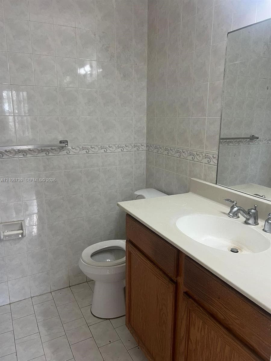 Bathroom featuring full-height wall tiling with decorative accent trim, vanity with integrated basin, polished metal faucet hardware, and wall-mounted mirror