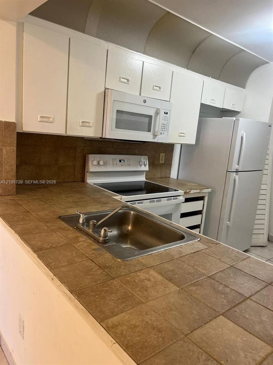 Kitchen featuring tiled countertops, stainless steel drop-in sink, white cabinetry, built-in microwave, and electric range