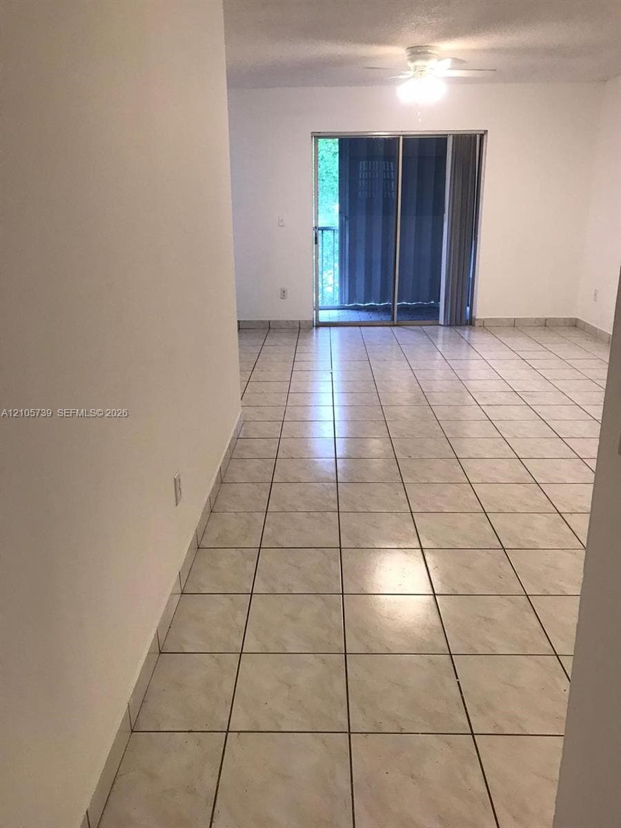 Ceramic tile flooring, white walls, and a sliding glass door with access to an exterior balcony, featuring a built-in ceiling fan with integrated lighting