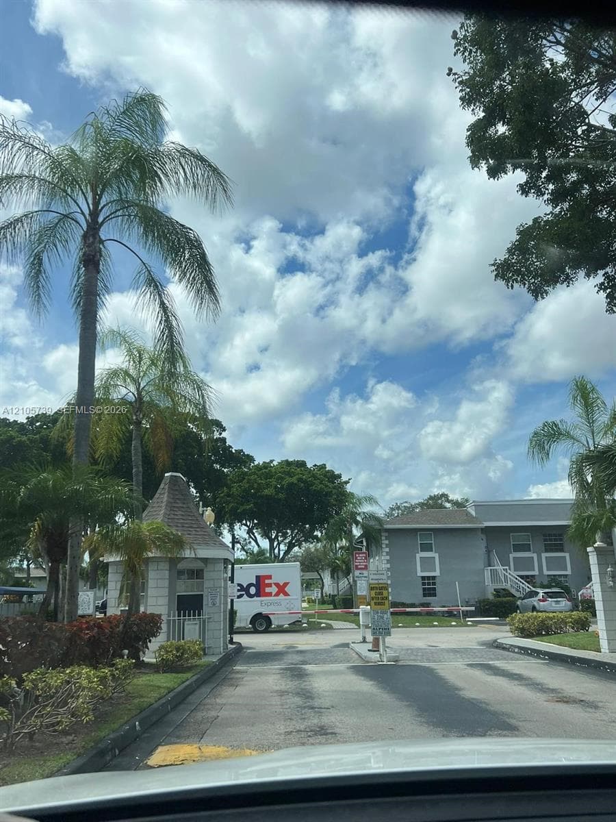 Gated entrance featuring a stone-clad guardhouse, asphalt driveway, and mature landscaping