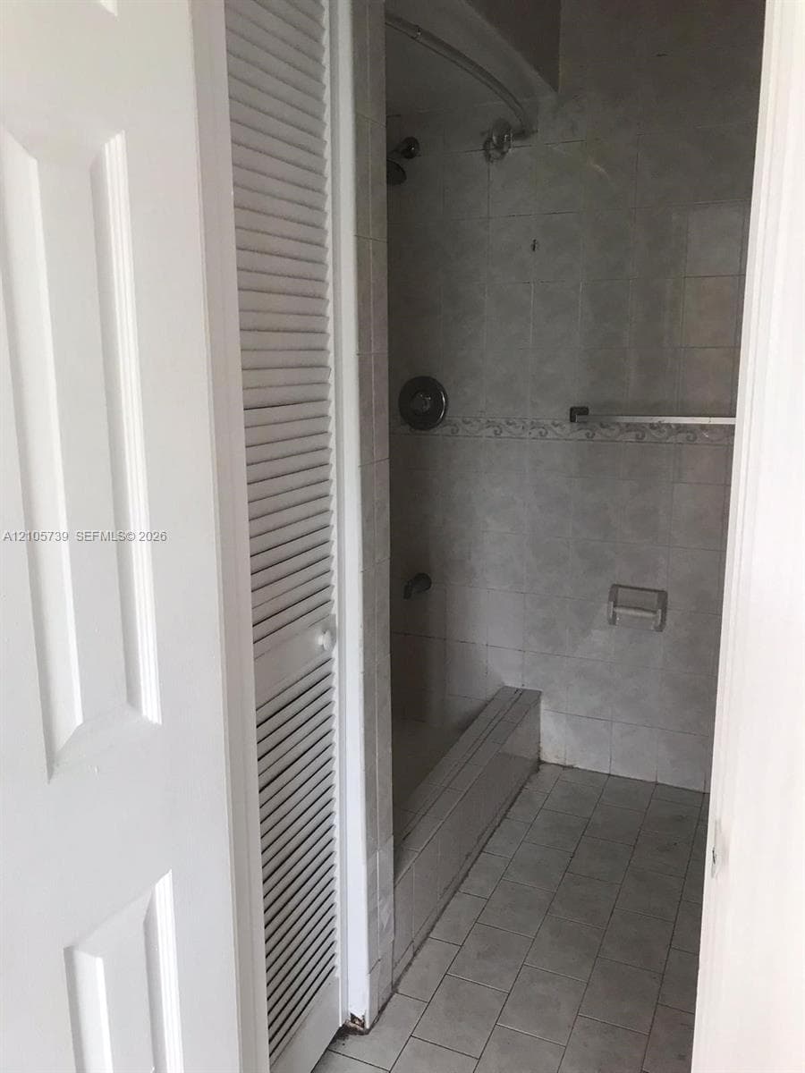 Shower area featuring floor-to-ceiling tile, an integrated tub surround, a curved shower rod, and louvered bi-fold doors