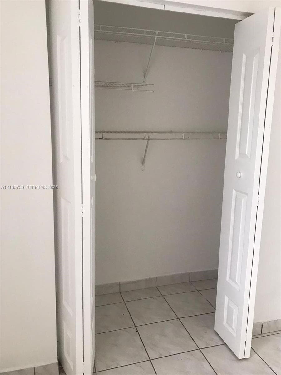 Reach-in closet featuring white paneled bifold doors, wire shelving, and neutral tile flooring