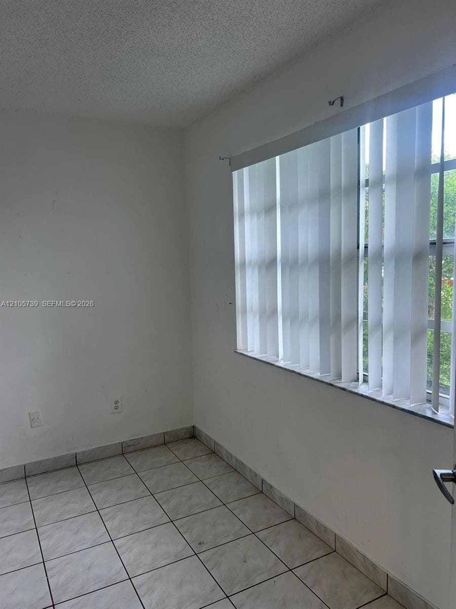 Interior space featuring neutral wall tones, ceramic tile flooring, and a window equipped with vertical blinds