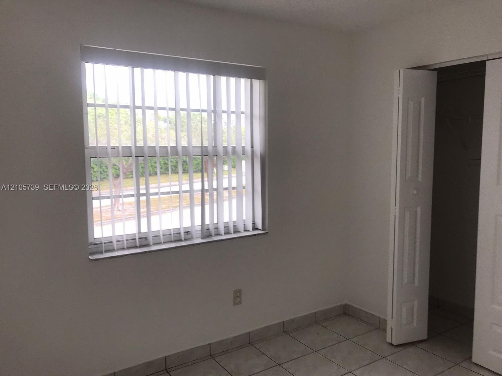 Neutral interior featuring large-format ceramic tile flooring, a window equipped with vertical blinds, and a closet with multi-panel bifold doors